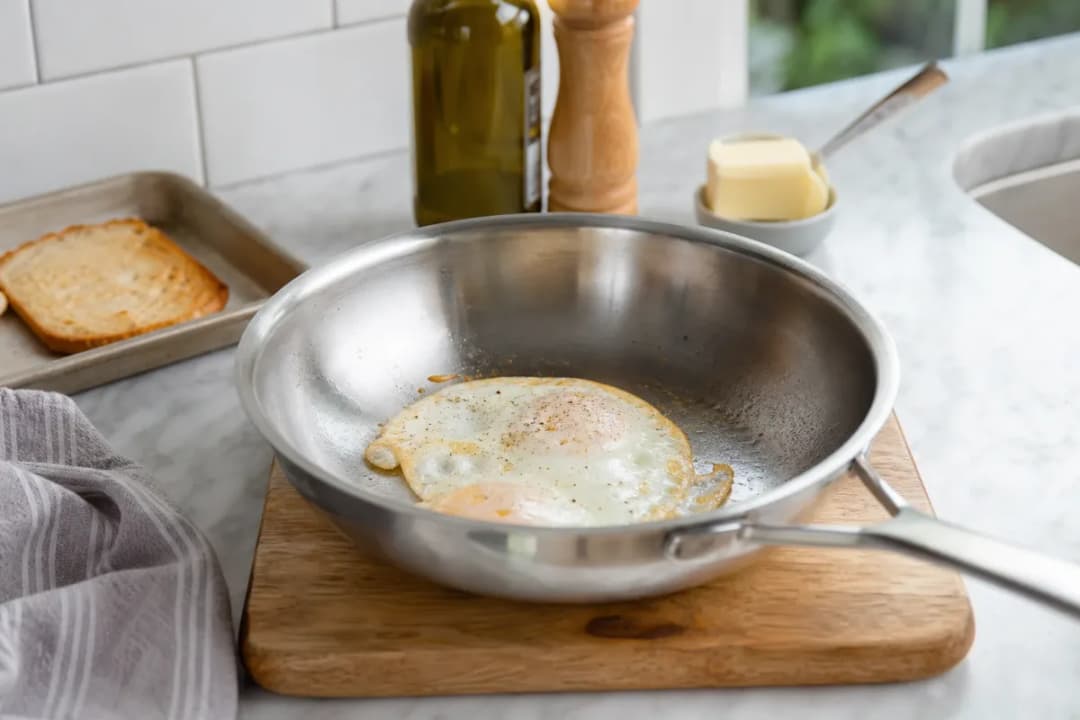 Editorial photo: How to Stop Eggs from Sticking to Stainless Steel Pans (quick fixes tip) — realistic home-kitchen scene with visible tools and ingredients in n