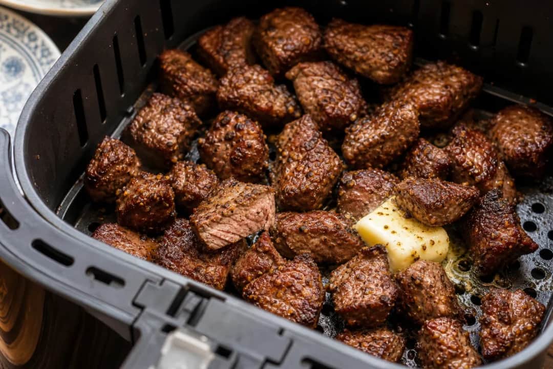 Plated steak bites drizzled with garlic butter sauce, garnished with fresh herbs.