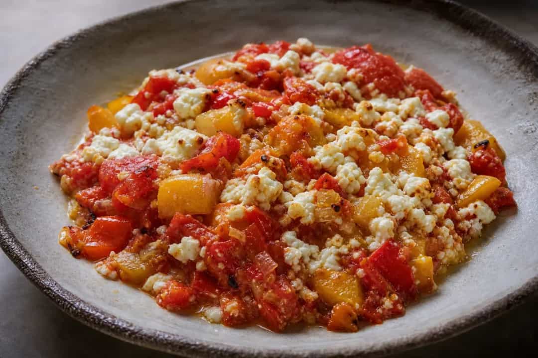 A vibrant plate of Albanian Fërgesë with colorful peppers, melted cheese, and a rich tomato sauce, garnished with fresh herbs.
