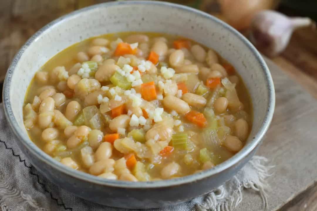 Thick white bean stew with vegetables, garnished with parsley in a bowl.