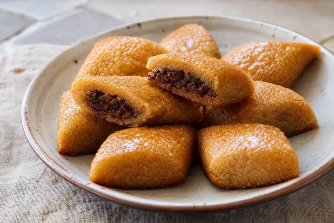 Golden-brown Algerian makroud pastries filled with sweet dates, drizzled with honey, served on a decorative plate.