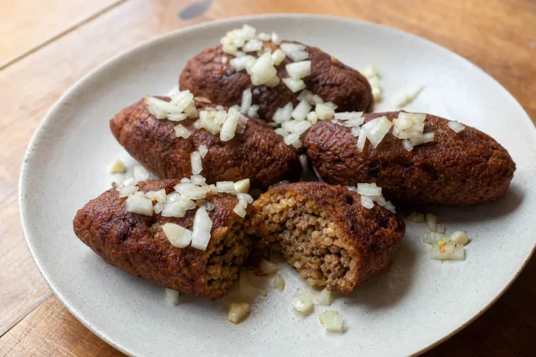 Golden-brown kyufta patties with bulgur and spiced beef, garnished with herbs on a white plate.
