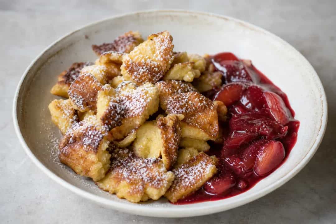 Fluffy shredded pancakes drizzled with plum compote and dusted with powdered sugar.