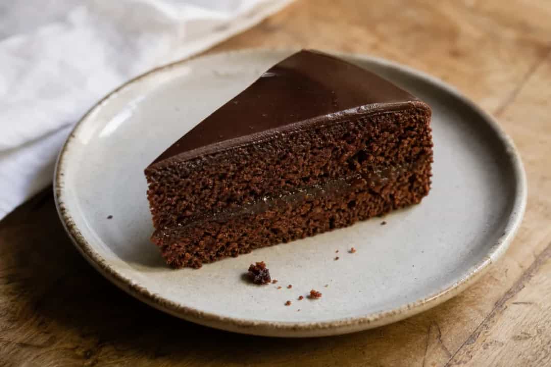 Rich chocolate layer cake with a glossy chocolate glaze and apricot jam filling, elegantly plated.