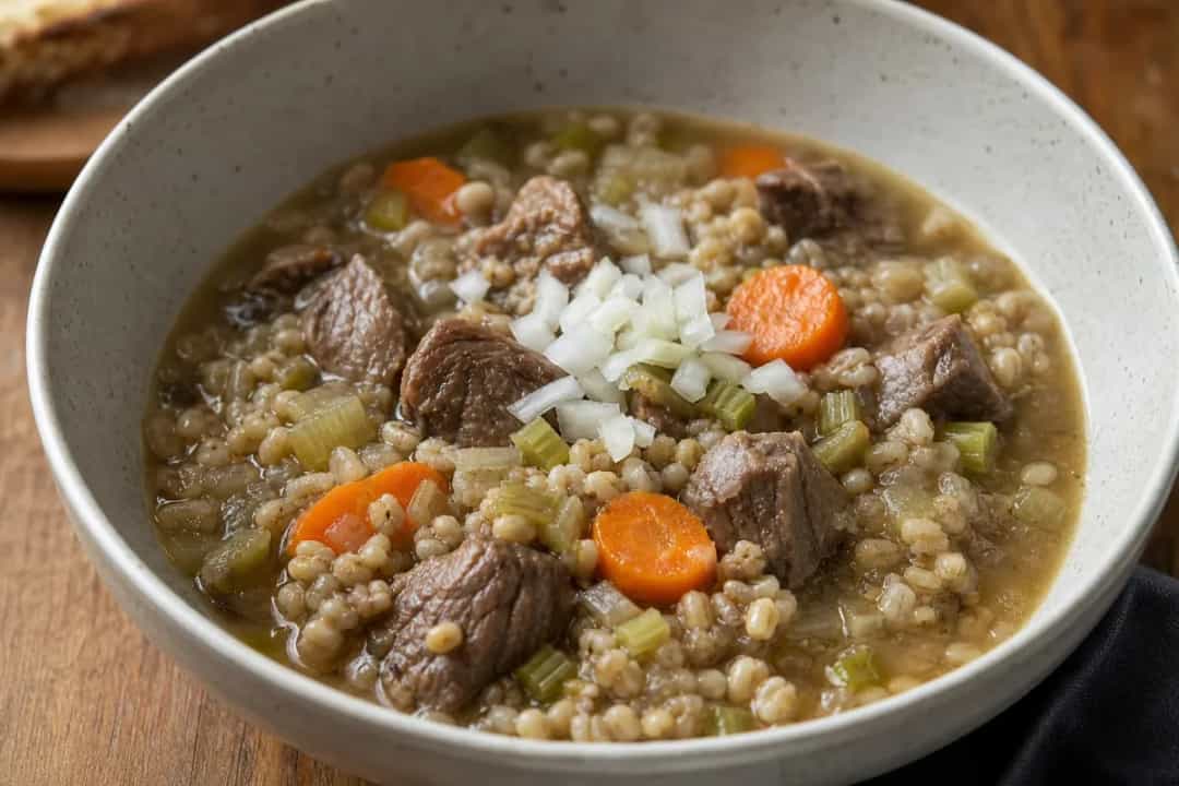 A bowl of Scotch broth with tender meat, barley, and colorful vegetables topped with fresh herbs.