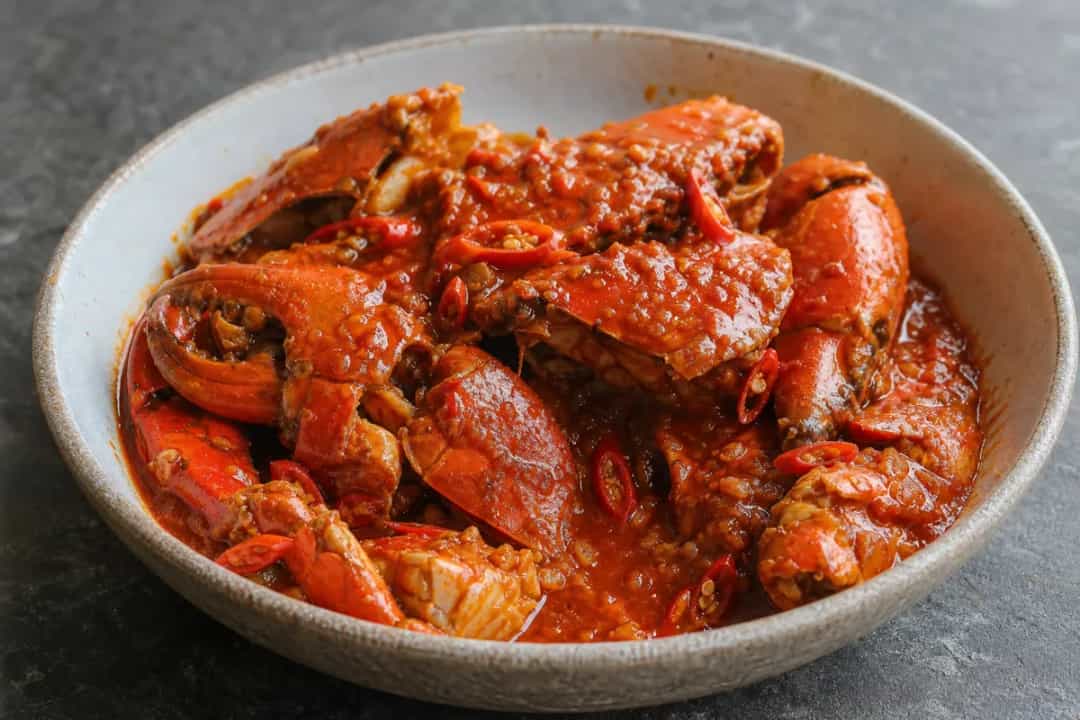 Plated Singaporean Chilli Crab with a glossy spicy sauce, garnished with coriander and served with bread for dipping.
