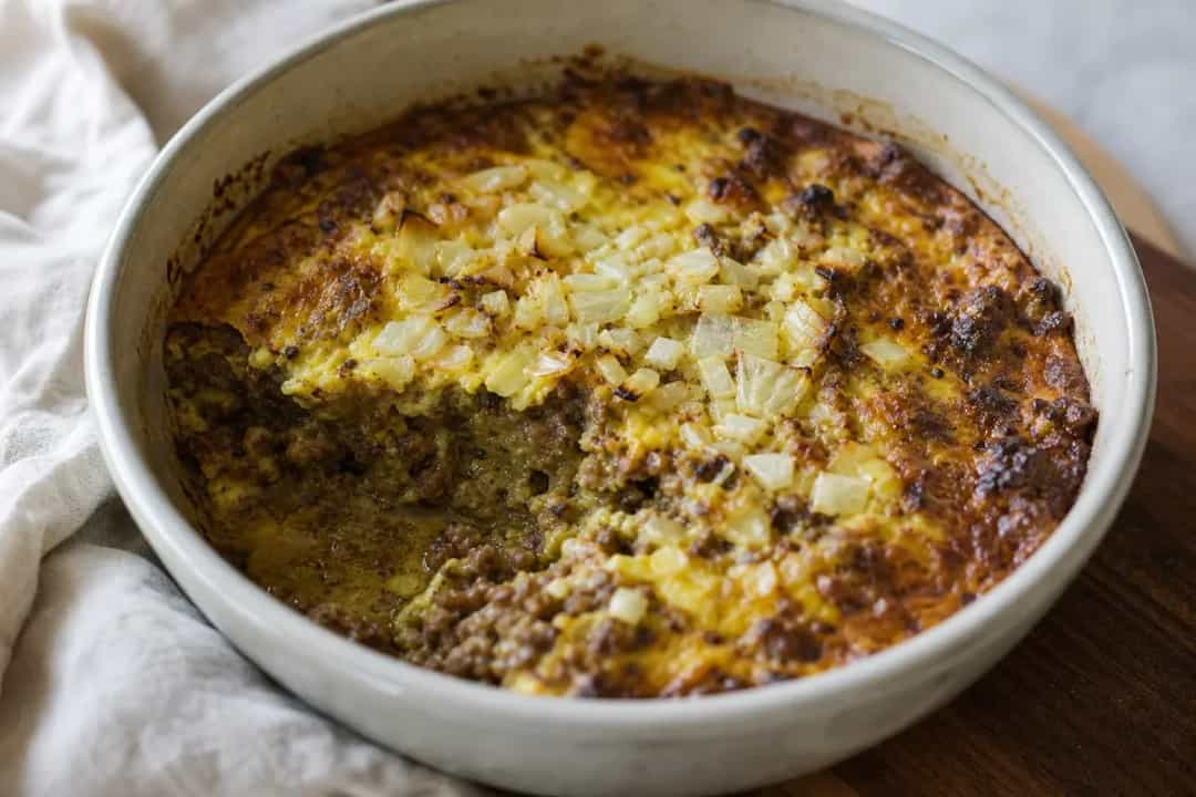 A slice of bobotie topped with golden egg custard, served with yellow rice and chutney.