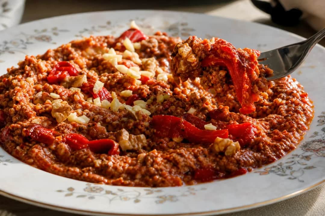 A bowl of spicy Muhammara dip garnished with walnuts and olive oil, served with fresh bread.