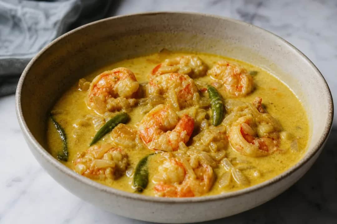 Creamy Chingri Malai Curry with prawns, coconut milk, and spices garnished with cilantro on a white plate.