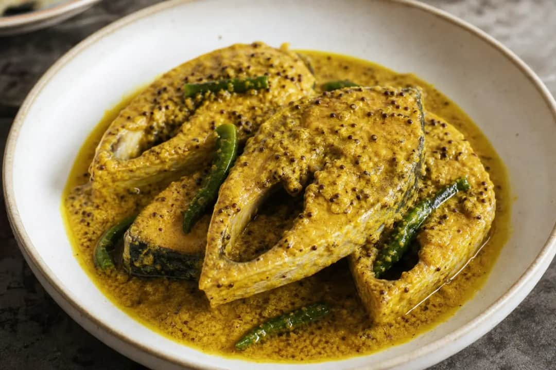 Plated Hilsa fish in a creamy mustard sauce, garnished with green chilies and served with rice.