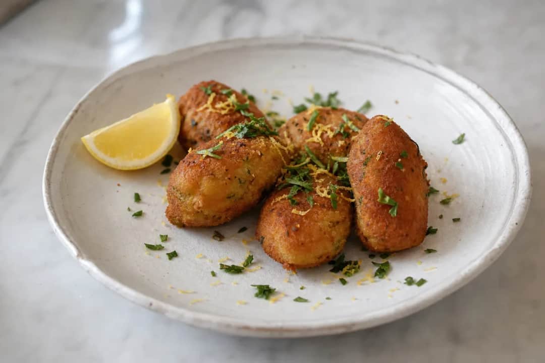 Golden brown shrimp croquettes garnished with fresh parsley and lemon wedges.