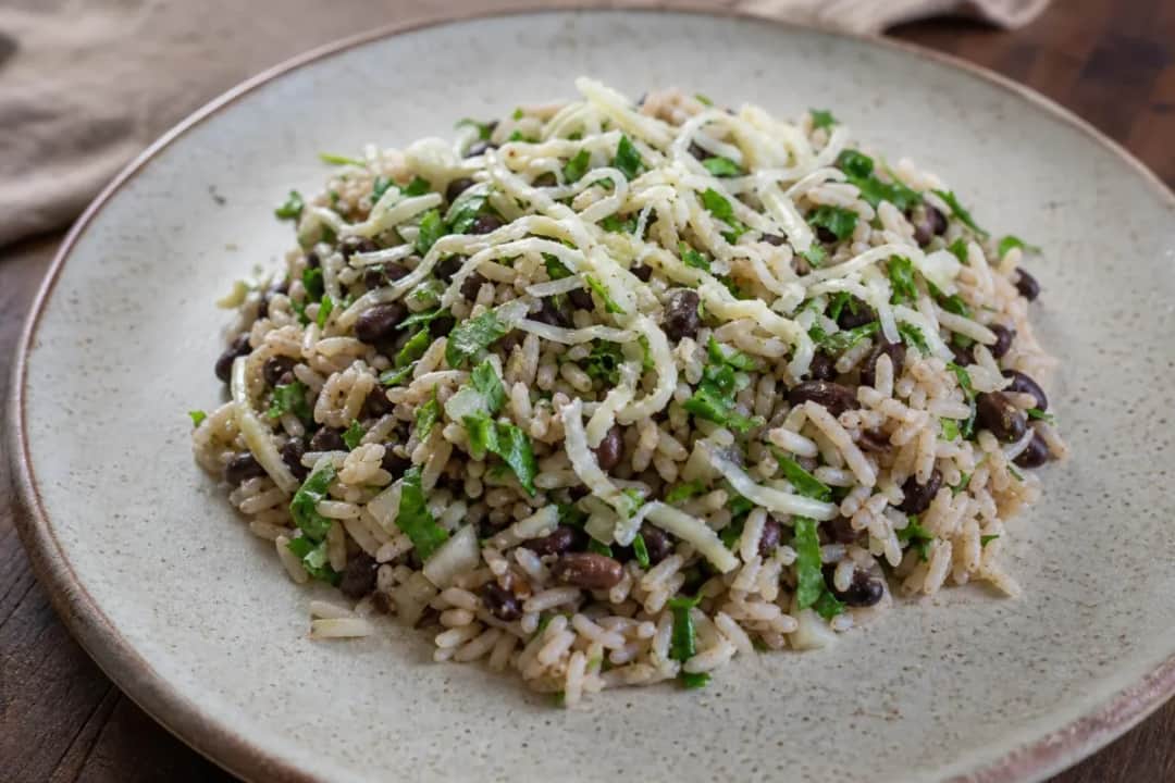 A colorful plate of Baião de Dois featuring fluffy rice, black beans, and melted cheese garnished with fresh herbs.