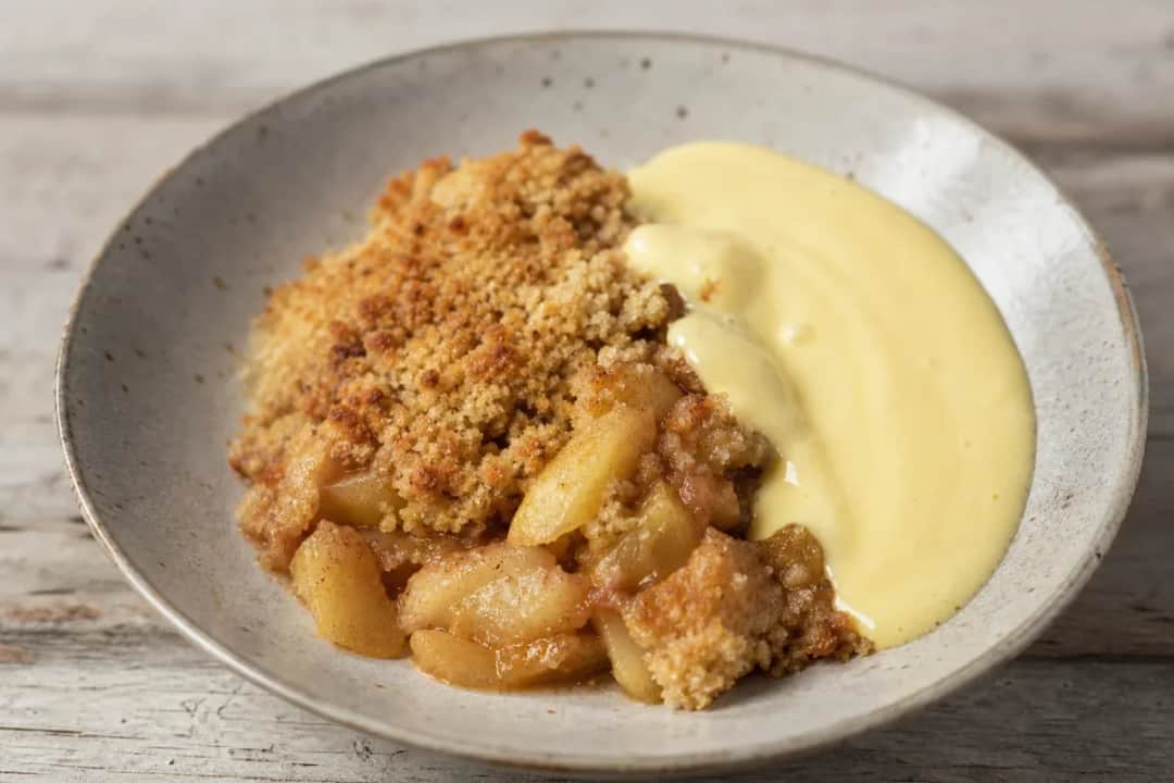Warm apple crumble topped with golden crust, served with creamy vanilla custard.