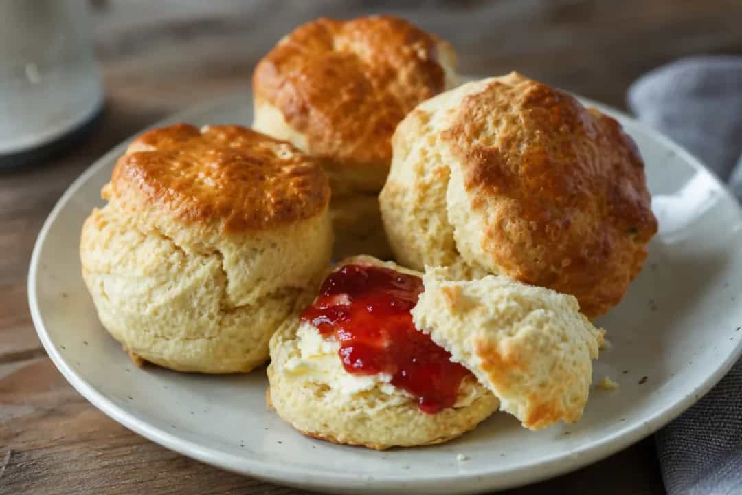Fluffy British scones topped with smooth clotted cream and bright strawberry jam, elegantly plated.