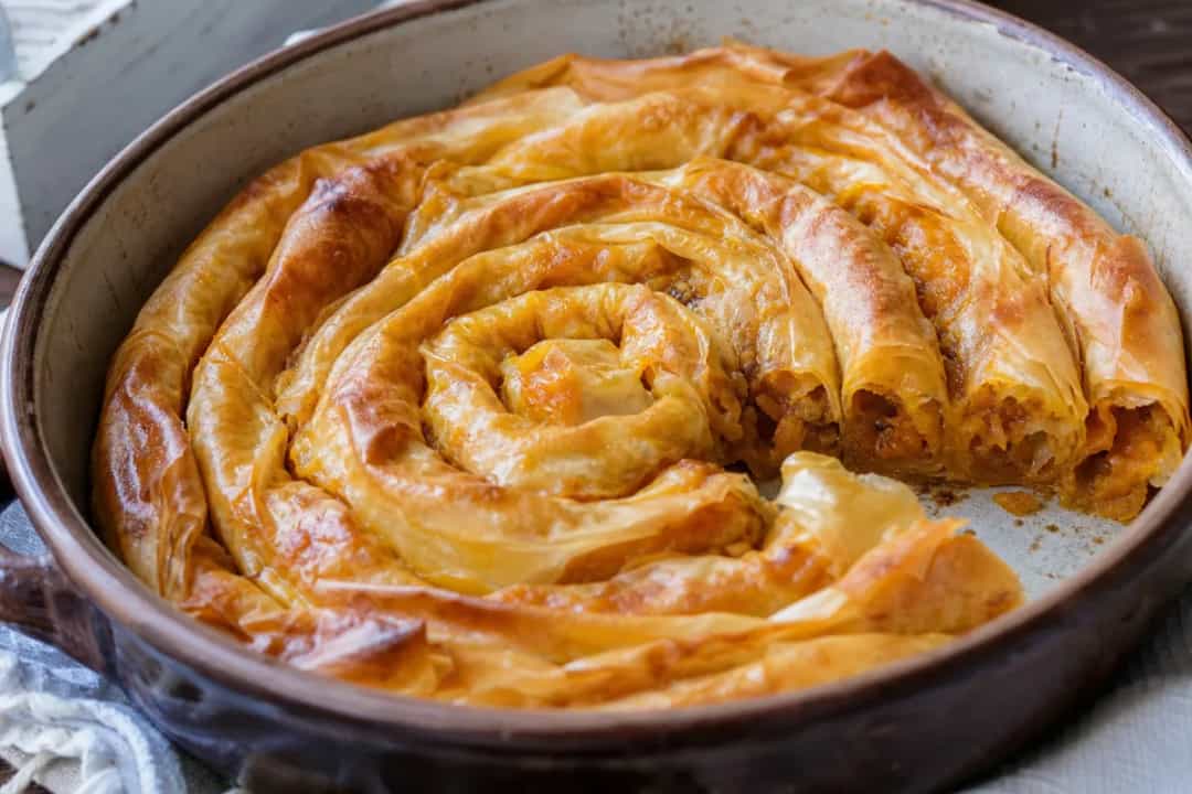 Golden-brown pumpkin strudel with flaky pastry, walnuts, and garnished with powdered sugar.