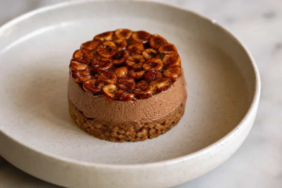 Layered hazelnut dessert with praline cream, garnished with chocolate and nuts.