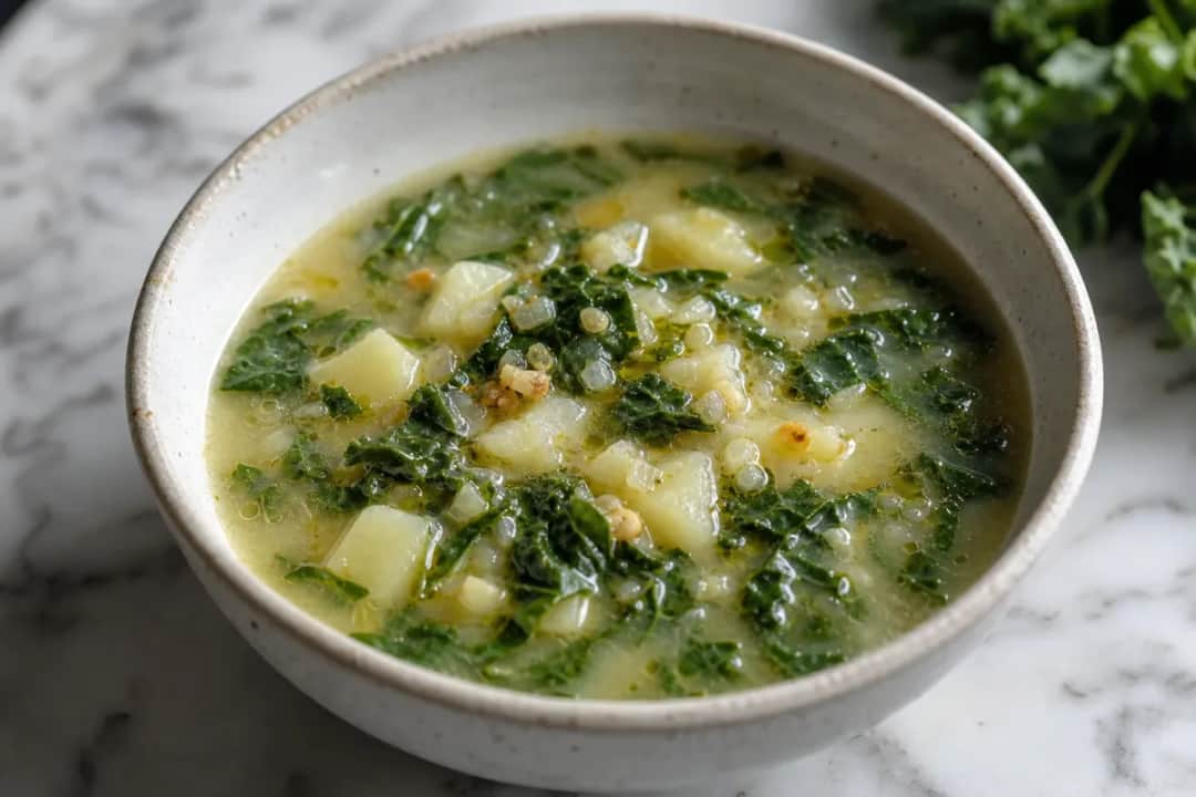 A bowl of Caldo Verde soup with vibrant green kale, creamy potatoes, and a drizzle of olive oil, garnished with slices of chorizo.