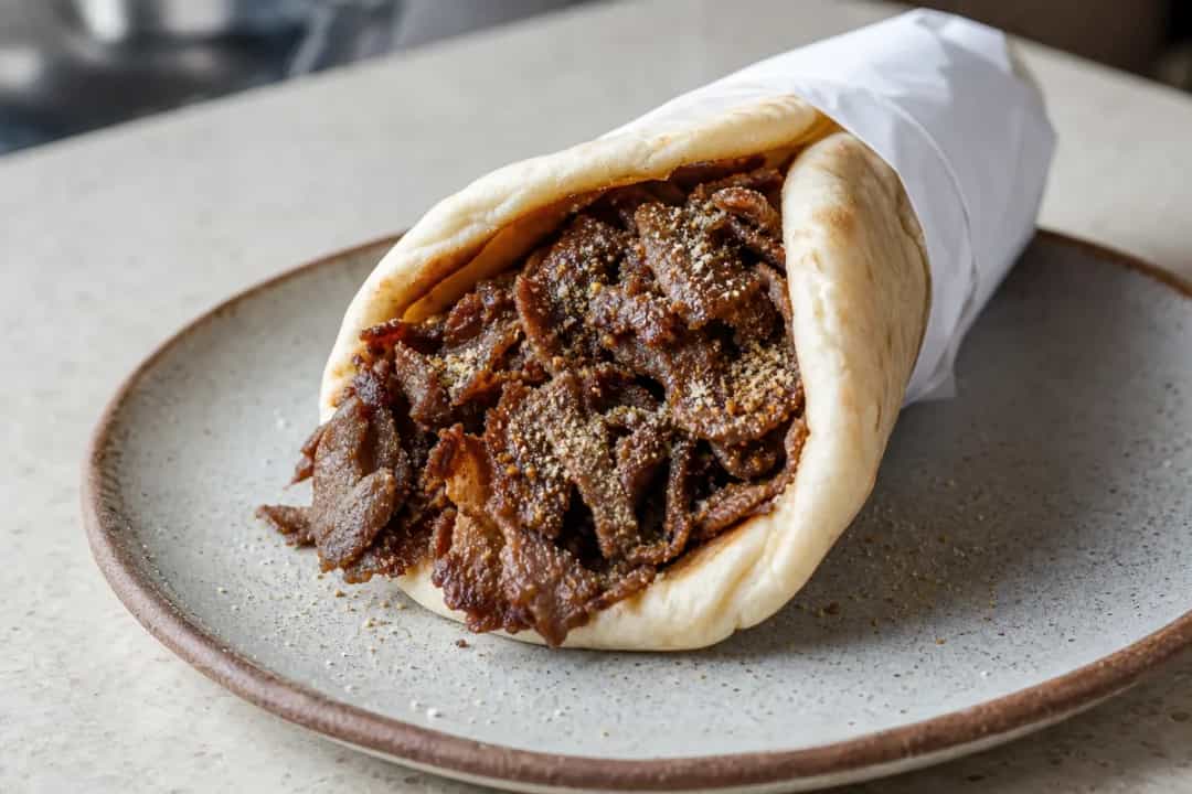 Plated Halifax Donair with tender beef, fresh veggies, and creamy sweet garlic sauce in pita bread.