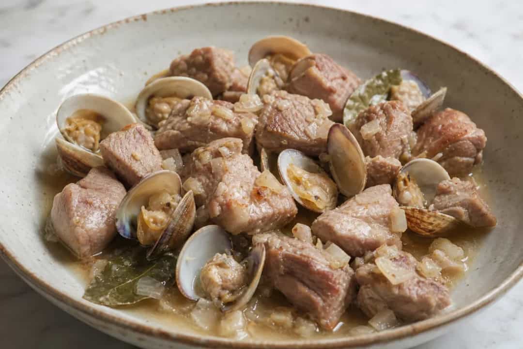 A plate of Carne de Porco à Alentejana with tender pork, clams, and herbs, garnished with fresh parsley.