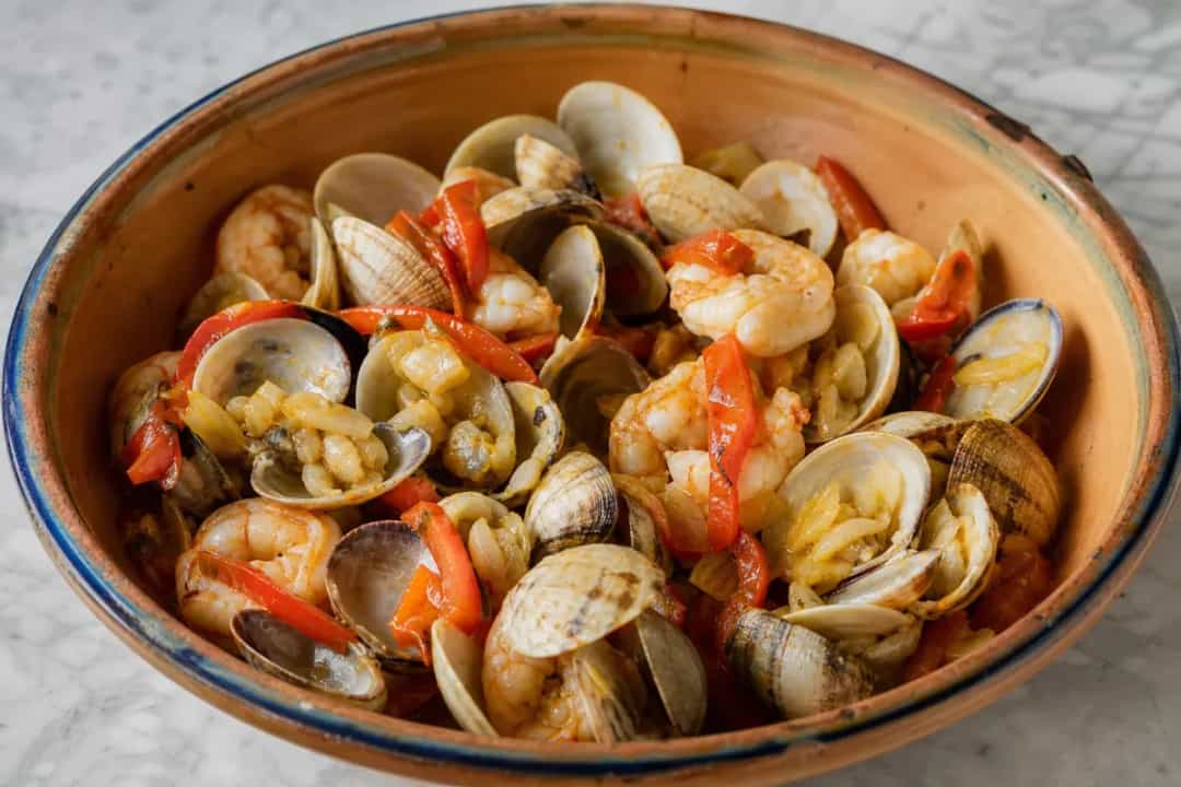 A vibrant seafood cataplana featuring clams, shrimp, and herbs, beautifully plated.