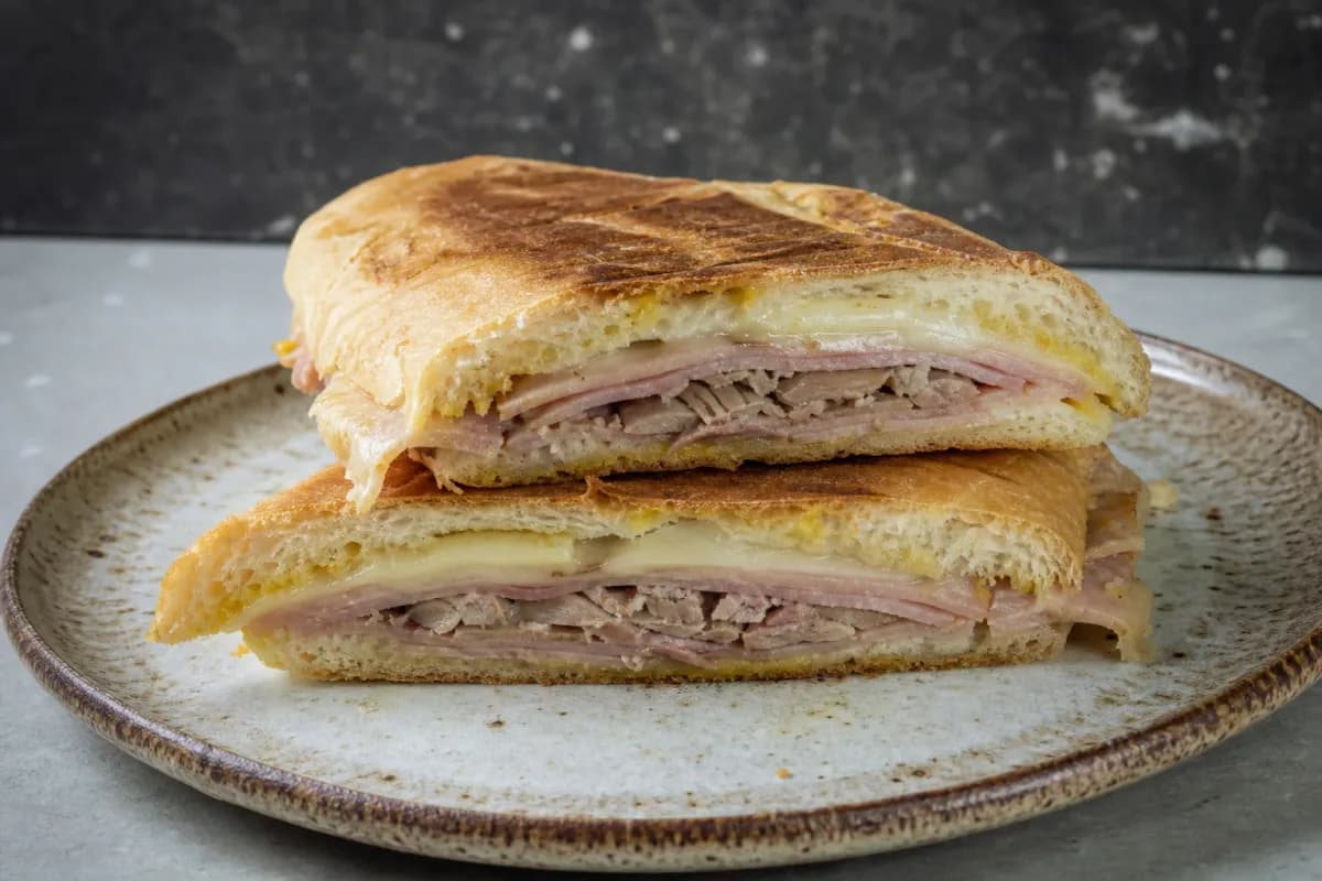 Toasted Cuban sandwich with layers of ham, roast pork, and melted Swiss cheese, golden brown crust.