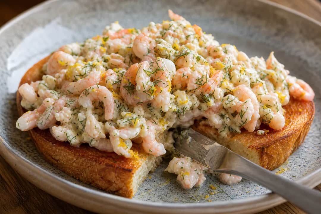 Plated Toast Skagen with creamy shrimp salad, dill, and lemon zest on toasted bread.