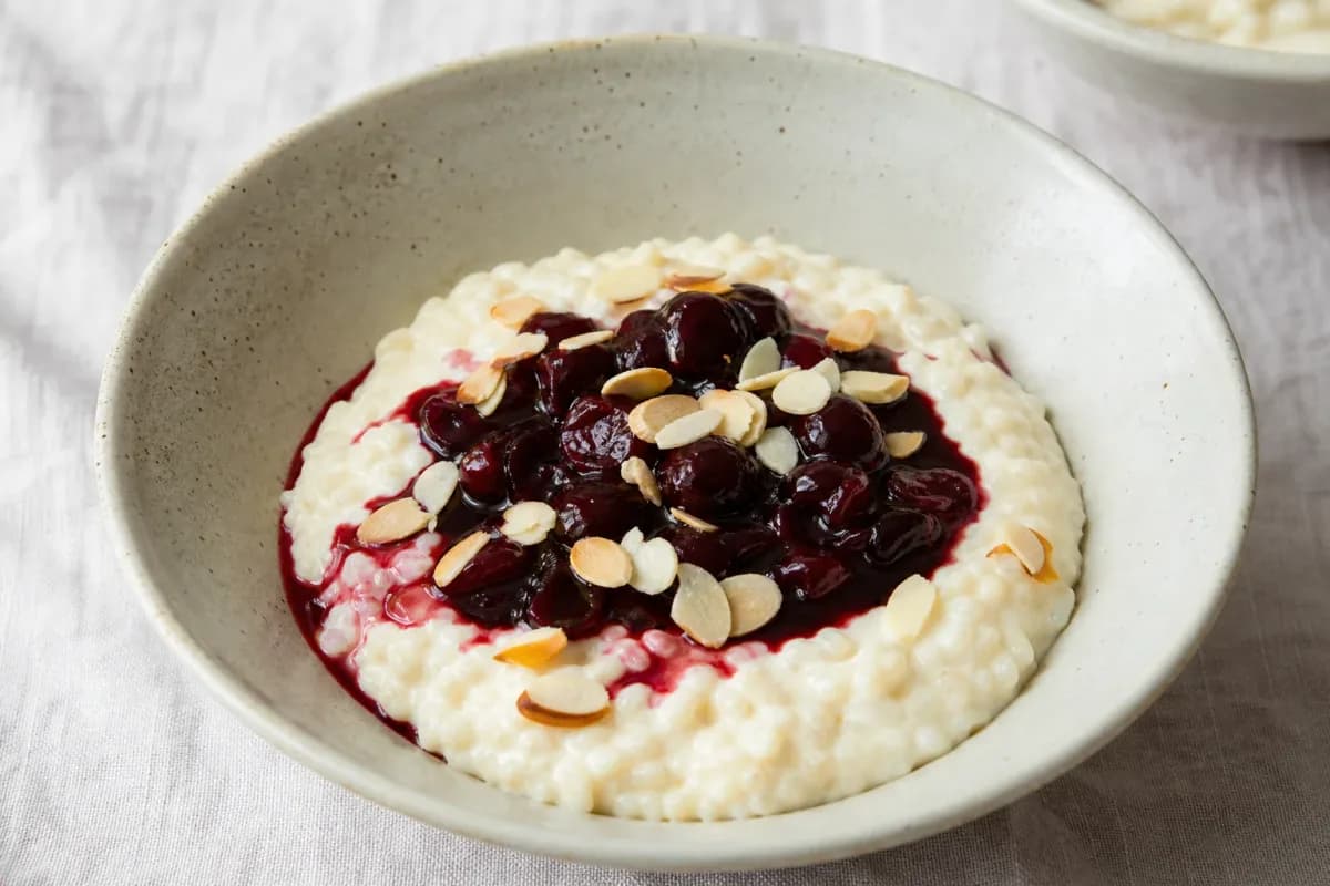 A bowl of creamy rice pudding topped with bright red cherry sauce and slivered almonds, garnished with mint.