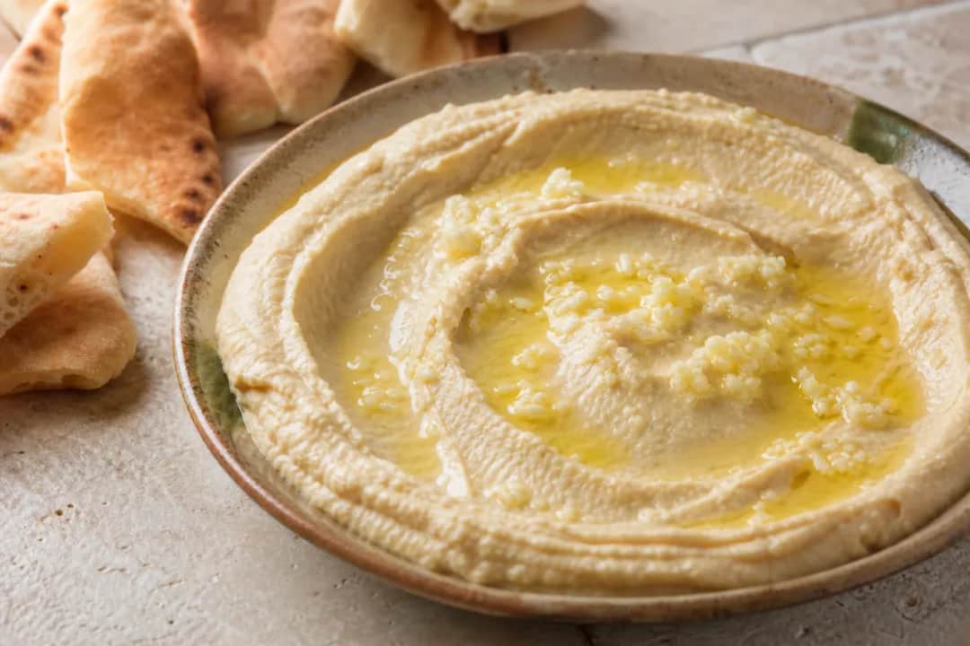 Smooth, creamy hummus garnished with olive oil and served with warm pita slices on the side.