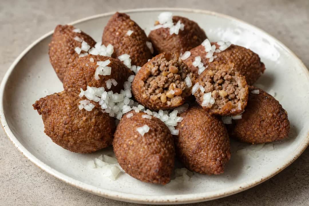 Golden-brown kibbeh with a crispy exterior, filled with spiced beef and pine nuts, garnished with parsley.