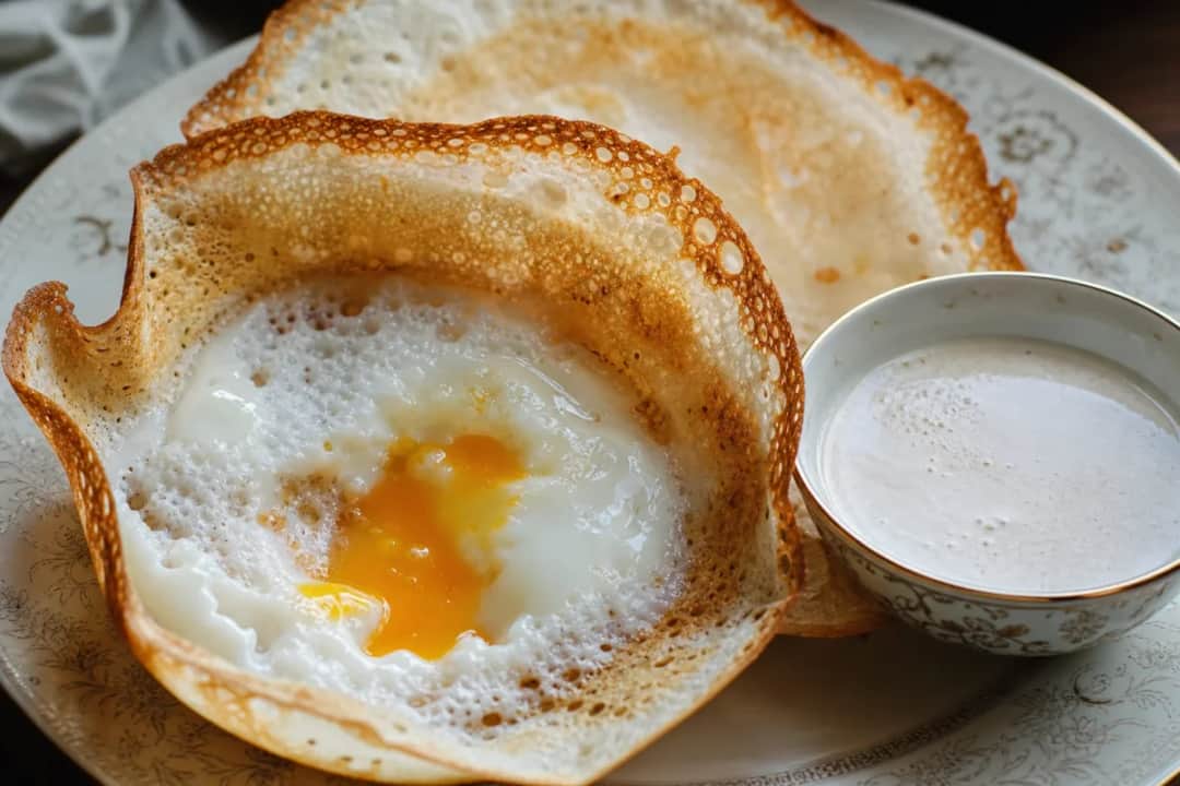 Crispy Sri Lankan egg hoppers served with a warm coconut sauce, showcasing a golden texture and soft egg center.