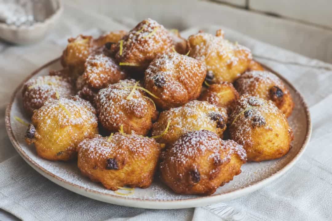 Golden-brown fritule dusted with powdered sugar, showcasing a fluffy texture and citrus zest.