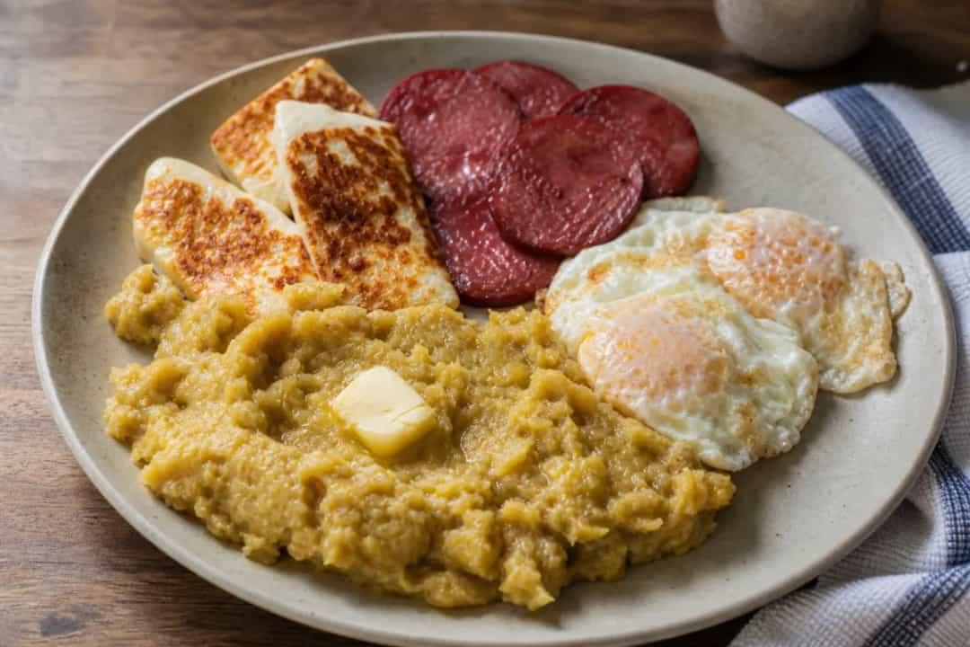 Plate of mangú topped with fried cheese and salami, served with sunny-side-up eggs.