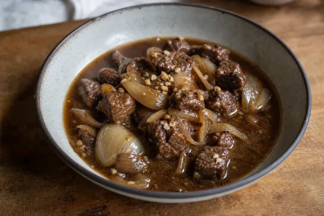Rich beef and onion stew garnished with fresh herbs in a rustic bowl.