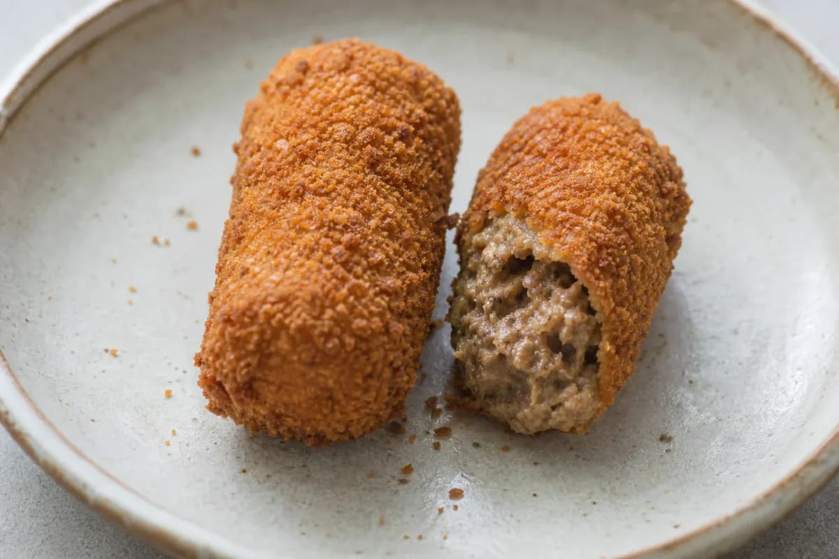 Crispy golden-brown kroketten filled with beef ragout, garnished and plated attractively.