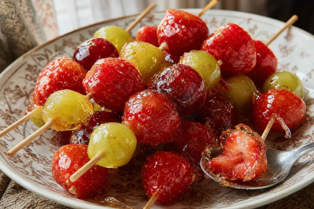Plated tanghulu with shiny, candied fruit on skewers, glistening syrup coating, and vibrant colors.