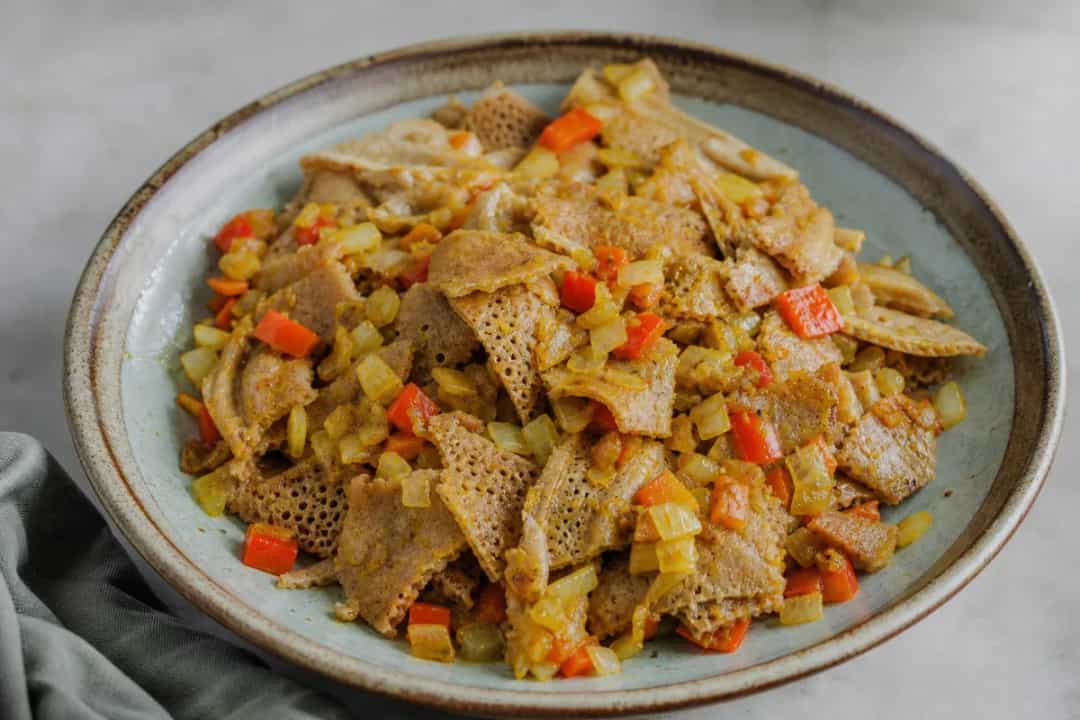 Bowl of Ethiopian Firfir with torn injera, spiced sauce, and fresh herbs garnishing the top.