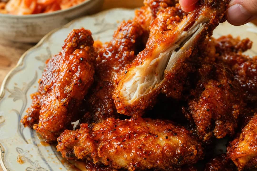 Plated extra crispy Korean fried chicken drizzled with spicy yangnyeom sauce, garnished with sesame seeds.