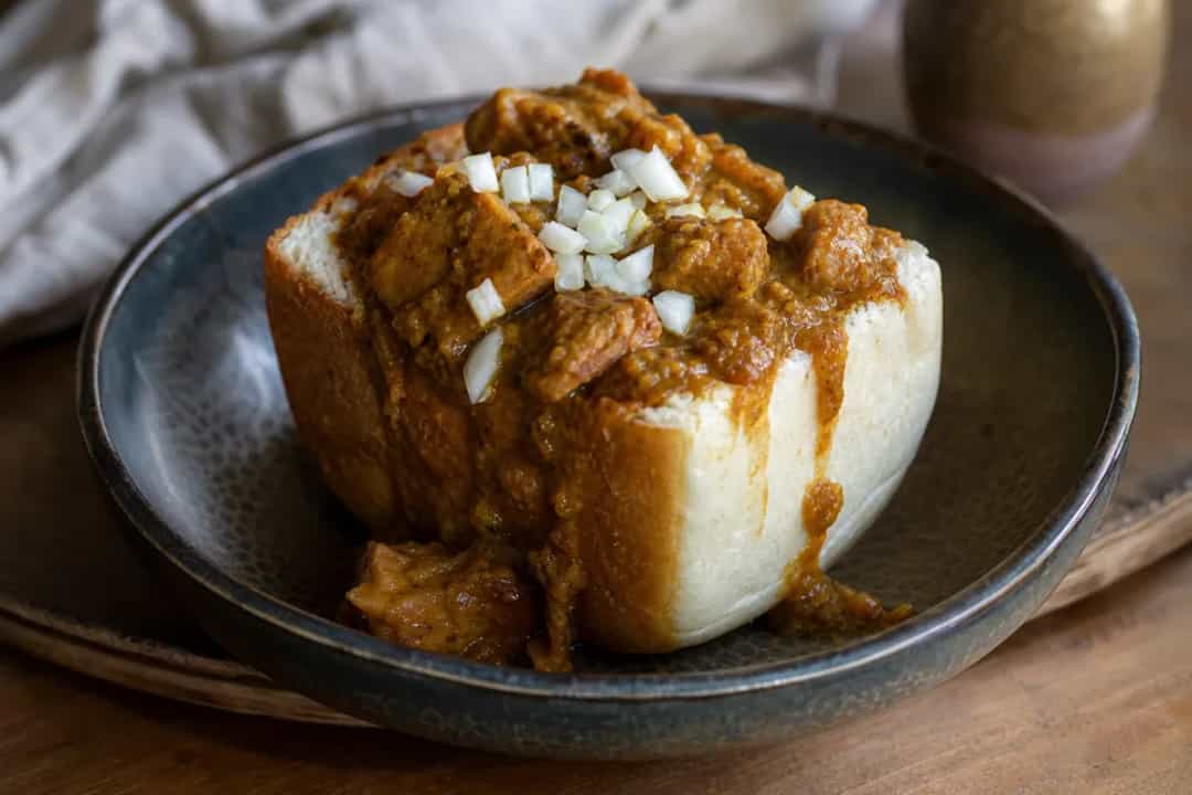 A hearty South African Bunny Chow with spicy chicken curry filling, served in a crusty bread bowl, garnished with fresh coriander.