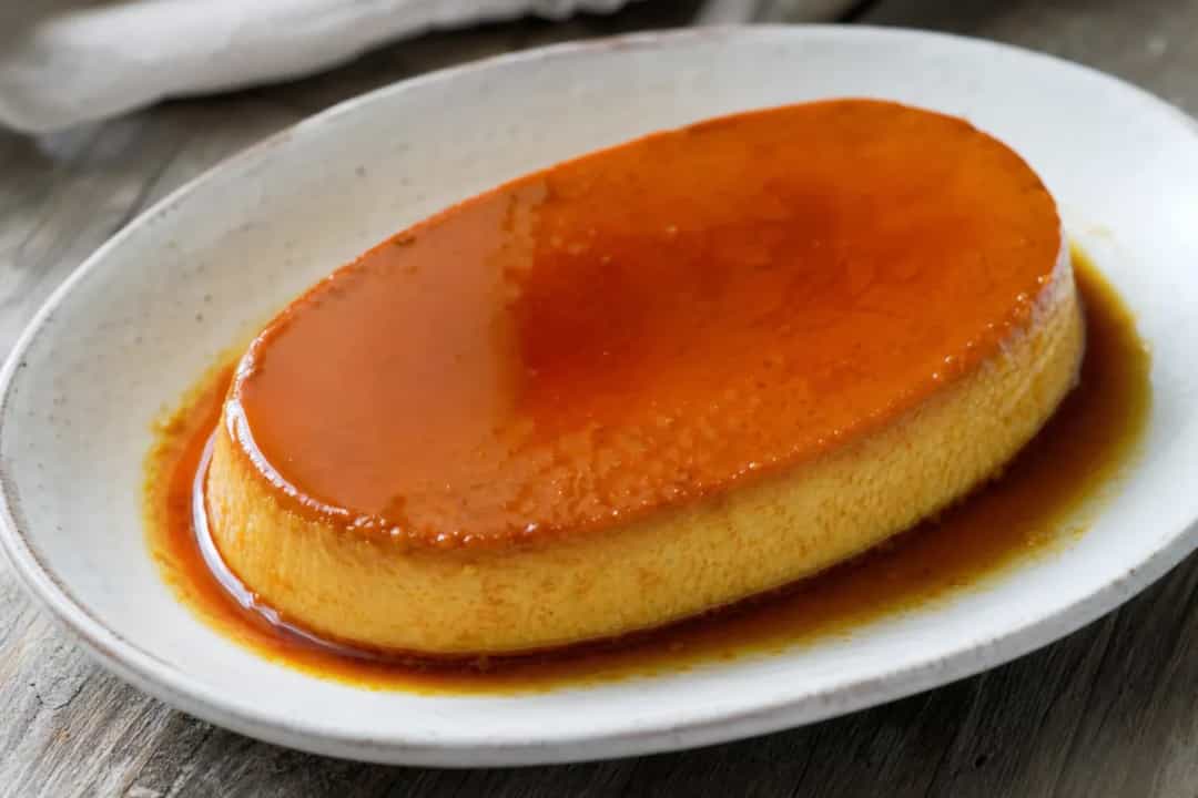 Smooth and creamy leche flan topped with glossy caramel, served in a round dish.