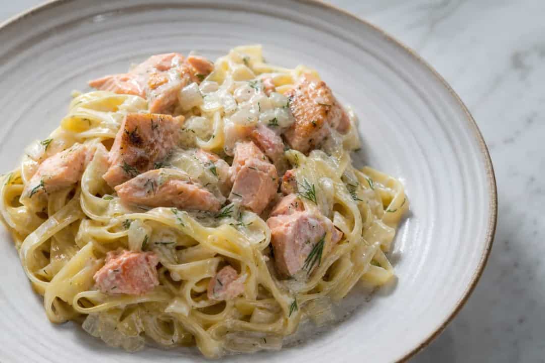Creamy salmon pasta garnished with fresh dill and garlic, beautifully plated.
