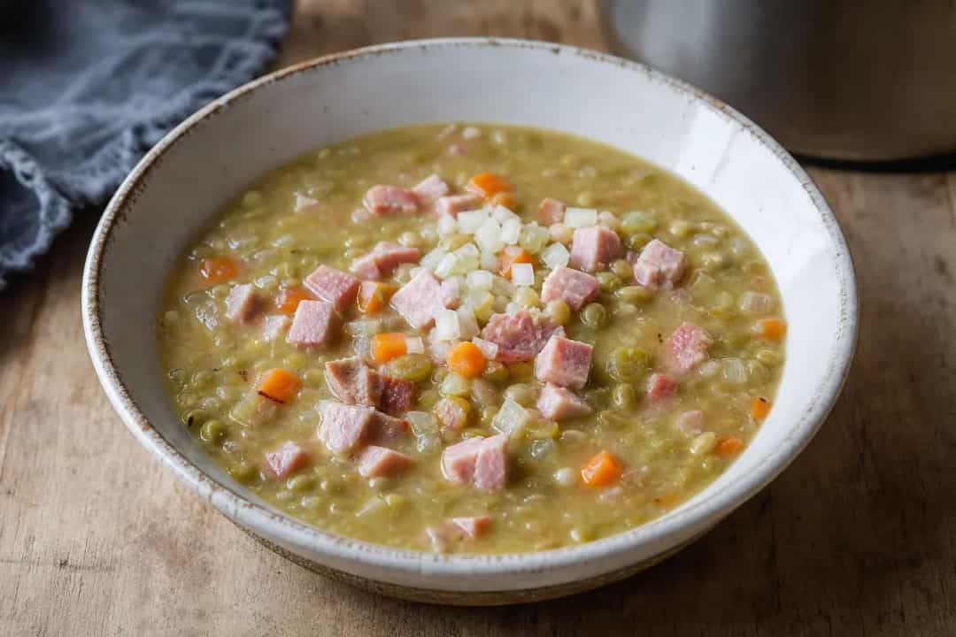 Creamy green pea soup topped with diced ham and a dollop of mustard, garnished with fresh parsley.