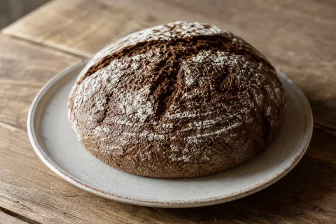 Rustic Finnish rye bread with a crusty exterior and scattered seeds, sliced and served on a wooden board.