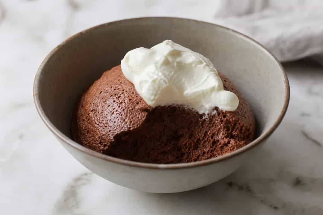 Smooth dark chocolate mousse topped with whipped cream and chocolate shavings, elegantly plated.