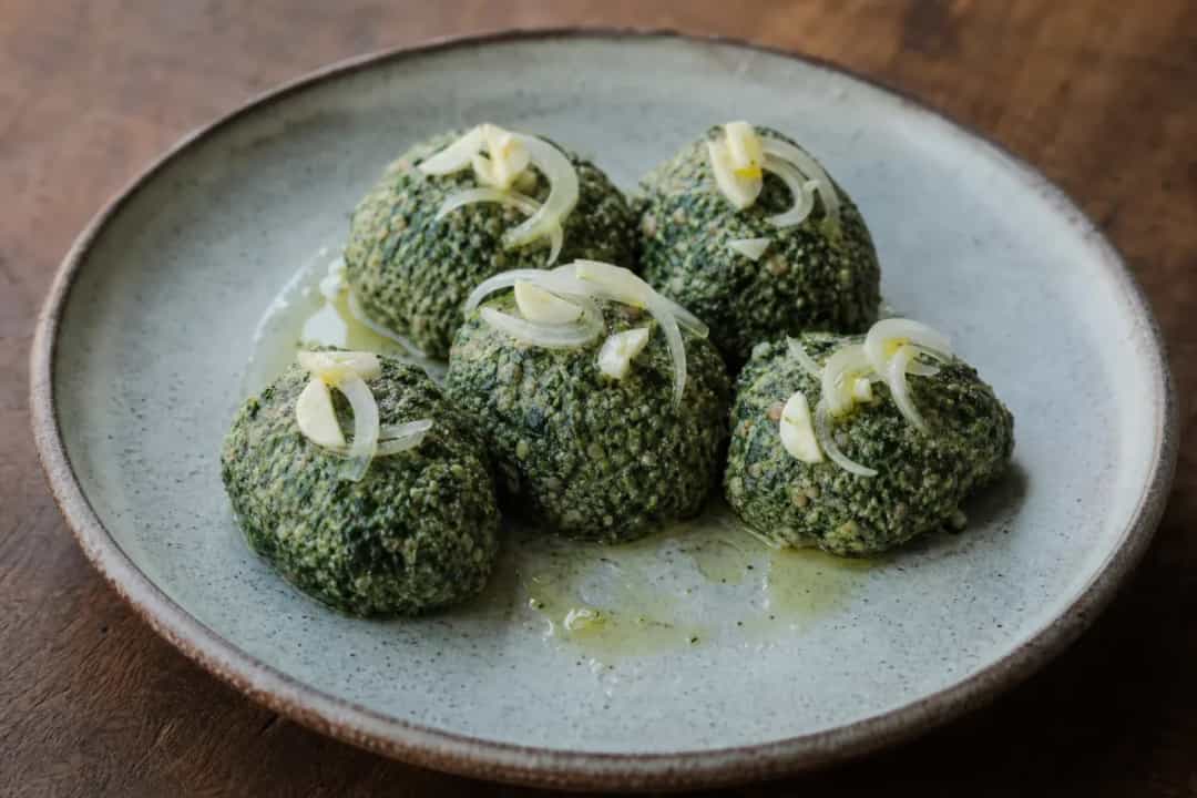 A vibrant dish of Georgian pkhali showcasing a green spinach and walnut mixture garnished with herbs and served in a bowl.