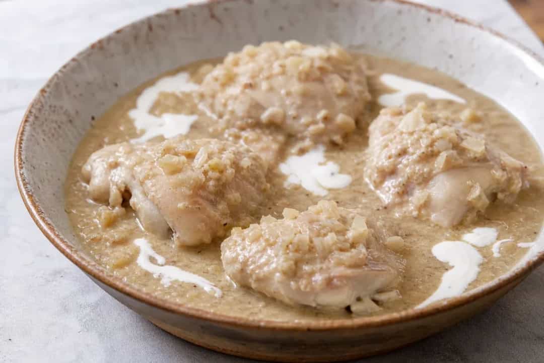 Tender chicken pieces coated in a creamy walnut sauce, garnished with herbs on a white plate.