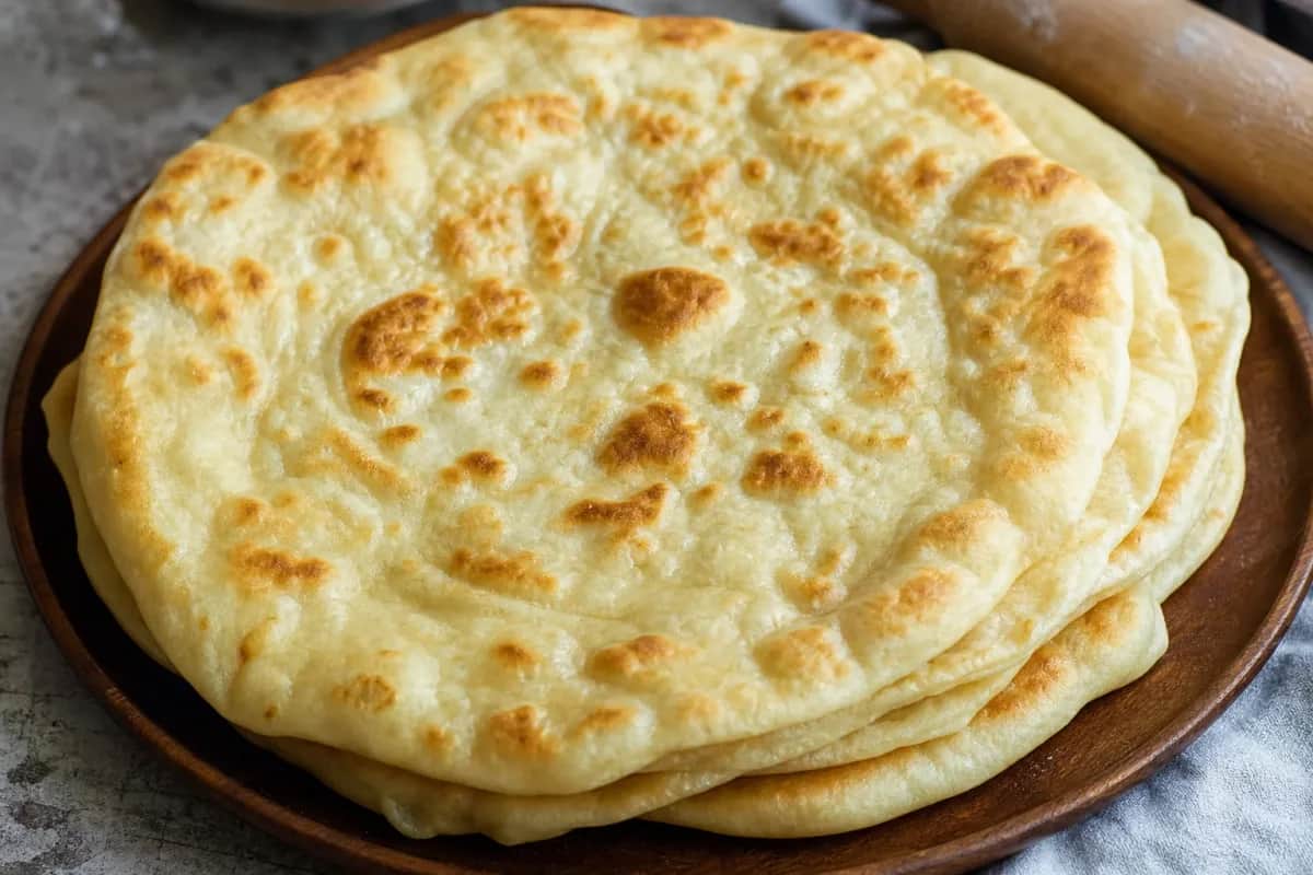 Golden Kazakh Shelpek flatbread with a soft texture, lightly browned and served on a wooden platter.