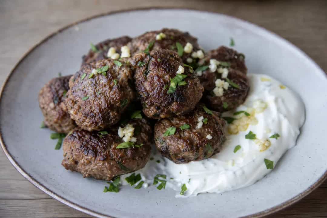 Crispy Greek keftedes garnished with herbs, served with garlic yogurt sauce on the side.