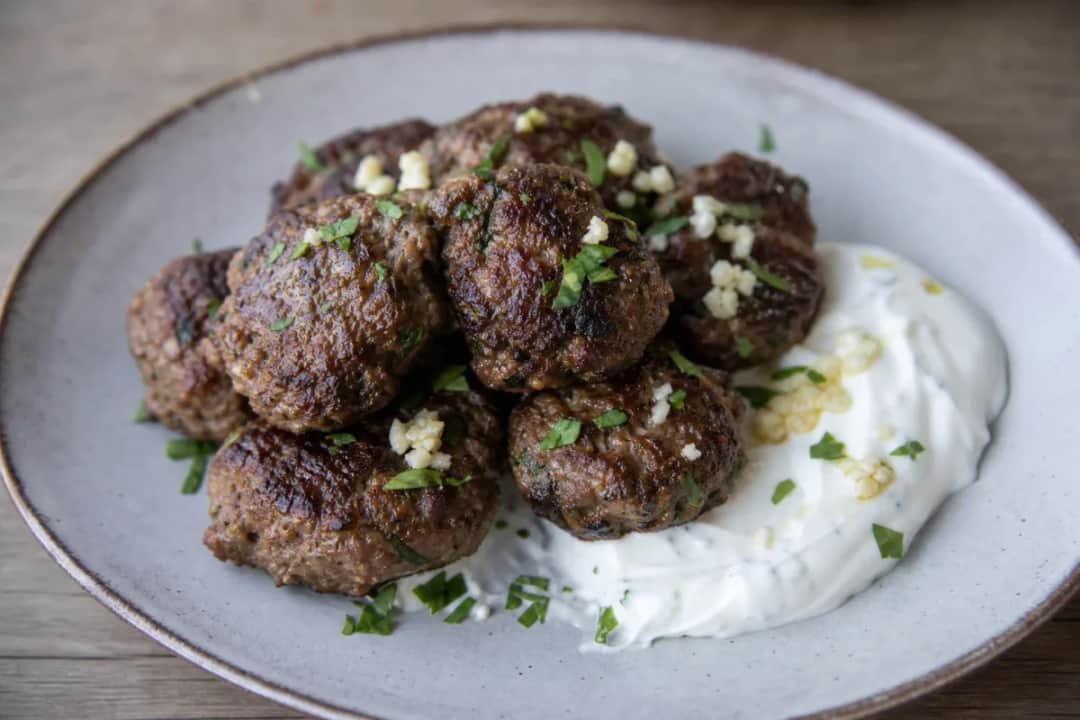 Crispy Greek keftedes garnished with herbs, served with garlic yogurt sauce on the side.