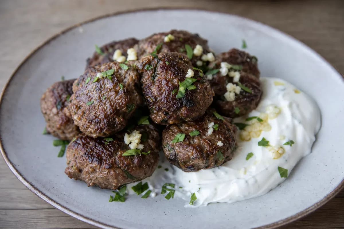 Crispy Greek keftedes garnished with herbs, served with garlic yogurt sauce on the side.