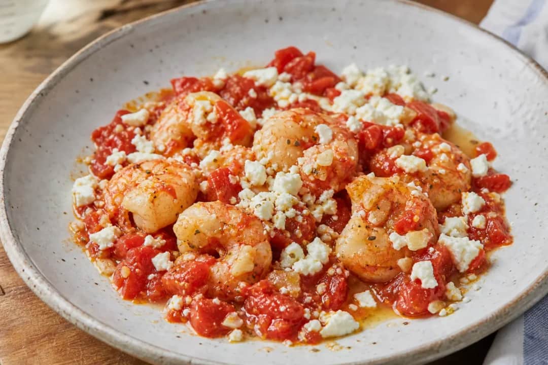 Plated shrimp saganaki with tomatoes and feta, garnished with parsley, showcasing a vibrant red sauce.